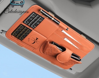 May include: Orange car visor organizer with multiple compartments for cards, pens, and other small items. Features a pen, cards, and the name "Jack" printed on the front. The organizer is designed to attach to a car visor.