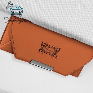 May include: A tan leather wallet with a silver clasp. The wallet features a black decorative design with the name "Geneva". The wallet is closed and appears to be new.