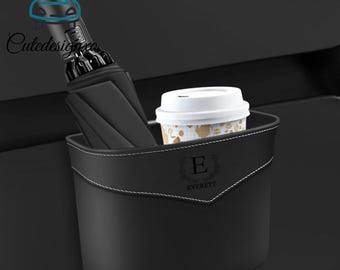 Può includere: Organizzatore per auto nero con cuciture bianche, contenente un ombrello nero e una tazza di caffè. L'organizzatore ha il nome "Everett" e la lettera "E". Progettato per l'auto.