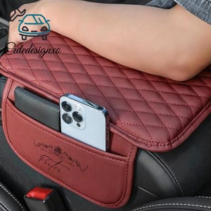 May include: A burgundy car seat organiser with a quilted pattern and a pocket. A smartphone and a wallet are visible in the pocket. The word "Porter" is printed on the pocket.