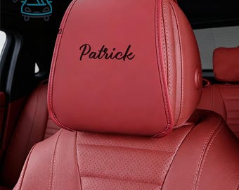 Può includere: Poggiatesta rosso per sedile auto con il nome "Patrick" in corsivo nero. Il poggiatesta è in pelle liscia cucita e fa parte di un sedile auto in pelle rossa.