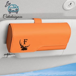 May include: An orange car visor organizer with a black deer head and the letter "F" printed on the front. The organizer is rectangular and has a strap for attaching to a car visor. The logo "Cutedesignxo" is in the upper left corner.