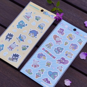 May include: Two sticker sheets featuring cartoon characters in various poses. One sheet is yellow, the other is light blue. The stickers depict characters in different activities, with a variety of colors including blue, green, and purple.