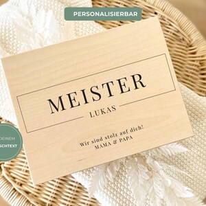 Könnte beinhalten: Eine hellfarbene Holzplakette mit dem Wort "MEISTER" in schwarzer Schrift, darunter "LUKAS". Die Plakette enthält auch den Text "Wir sind stolz auf dich! MAMA & PAPA". Die Wörter "PERSONALISIERBAR" und "MIT DEINEM WUNSCHTEXT" sind ebenfalls sichtbar.
