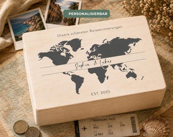Può includere: Una scatola rettangolare in legno chiaro con una mappa del mondo grigio scuro stampata sul coperchio. Il testo riporta "Unsere schönsten Reiseerinnerungen", "Sophia & Lukas" e "EST. 2025". La scatola ha una finitura liscia e un coperchio.