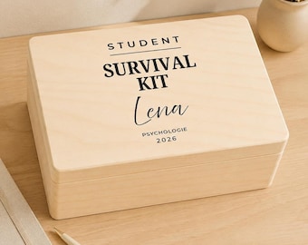 Può includere: Una scatola rettangolare in legno chiaro con coperchio incernierato. La parte superiore riporta la scritta STUDENT SURVIVAL KIT, il nome Lena e il testo PSYCHOLOGIE 2026. Una piccola etichetta verde in alto a sinistra mostra la parola PERSONALISIERBAR.