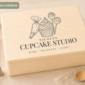 Könnte beinhalten: Eine rechteckige Holzkiste in hellem Farbton mit einer schwarzen Strichzeichnung eines Cupcakes, eines Spritzbeutels und Cake Pops. Der Text lautet NICOLES CUPCAKE STUDIO und BAKE DECORATE ENJOY. Ein grünes Etikett zeigt das Wort PERSONALISIERBAR.