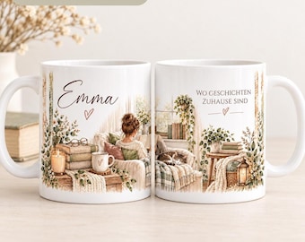 Può includere: Due tazze in ceramica bianca con un'illustrazione stampata di una persona che legge in una stanza accogliente con un gatto, libri e piante. La tazza sinistra mostra il nome Emma e un cuore, quella destra il testo Wo Geschichten Zuhause sind.