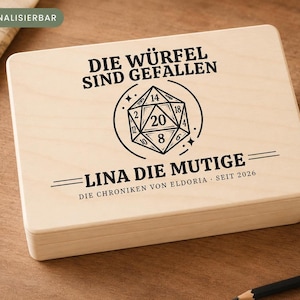 Könnte beinhalten: Eine rechteckige, helle Holzbox mit einer schwarzen Gravur eines zwanzigseitigen Würfels. Der Text lautet: DIE WÜRFEL SIND GEFALLEN, LINA DIE MUTIGE und DIE CHRONIKEN VON ELDORIA - SEIT 2026. Ein kleines grünes Etikett zeigt PERSONALISIERBAR.