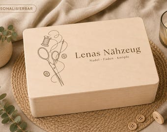Può includere: Una scatola rettangolare in legno chiaro con un'incisione marrone scuro raffigurante forbici da cucito, un rocchetto di filo e bottoni. Il testo recita "Lenas Nähzeug" seguito da "Nadel - Faden - Knöpfe" in un carattere serif scuro.