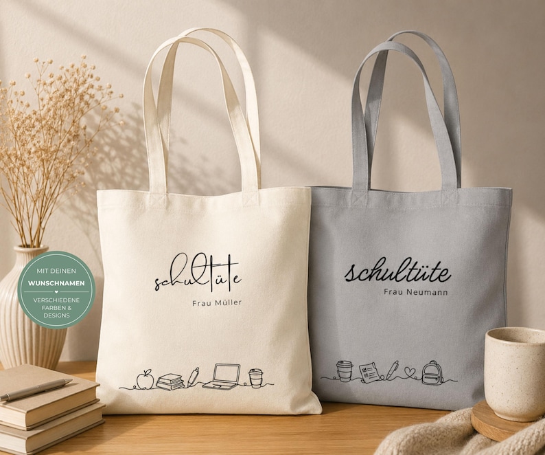 K&ouml;nnte beinhalten: Zwei Tragetaschen aus Canvas, eine cremefarbene und eine graue, mit schwarzer Schrift "Schult&uuml;te" und einem Namen darunter. Die cremefarbene Tasche hat eine Strichzeichnung von Schulmaterial. Die graue Tasche hat ein &auml;hnliches Design. Beide haben lange Henkel.