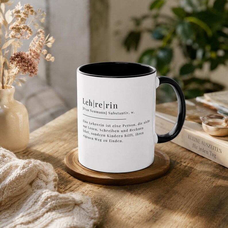 May include: A white ceramic mug with a black interior and handle, featuring black printed text that defines the German word Leh|re|rin, including the phonetic breakdown and a descriptive sentence about the role of a teacher in German.
