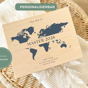Könnte beinhalten: Holztafel mit Weltkarten-Design in Marineblau. Der Text "MASTER 2026" ist zentriert, mit "You did it!" darüber. Zusätzlicher Text enthält "Lieber Lukas, wir sind stolz auf dich! Mama & Papa" und "MIT DEINEM WUNSCHTEXT".