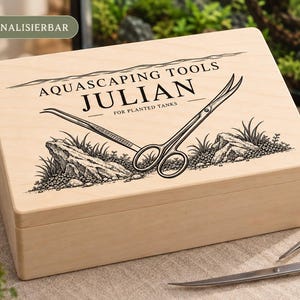 Könnte beinhalten: Eine rechteckige, helle Holzbox mit einer schwarzen Gravur von Aquascaping-Werkzeugen, Steinen und Pflanzen. Der Text lautet AQUASCAPING TOOLS, JULIAN und FOR PLANTED TANKS. Die Box liegt neben einer Metallschere und einer Pinzette.