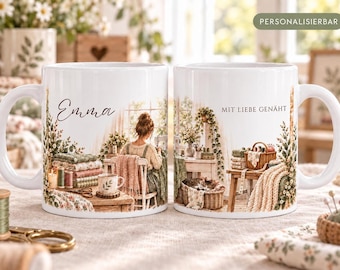 Può includere: Due tazze in ceramica bianca con un'illustrazione stampata di una persona che cuce in una stanza soleggiata. Una tazza riporta il nome Emma, l'altra il testo tedesco MIT LIEBE GENÄHT. La scena include pile di tessuti, un gatto e piante.