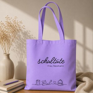 K&ouml;nnte beinhalten: Eine lavendelfarbene Tragetasche mit schwarzem Text, der "schult&uuml;te Frau Neumann" lautet. Unter dem Text befindet sich eine Strichzeichnung einer Kaffeetasse, einer Checkliste, eines Stifts, eines Herzens und eines Rucksacks. Die Tasche hat zwei Griffe.