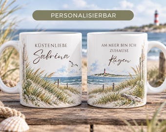 Può includere: Due tazze in ceramica bianca con un'illustrazione di un paesaggio costiero con dune di sabbia, erba di spiaggia e un faro. La tazza sinistra mostra il testo KÜSTENLIEBE Sabrina, quella destra AM MEER BIN ICH ZUHAUSE Rügen. Il banner superiore riporta PERSONALISIERBAR.