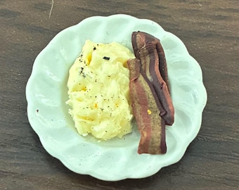 May include: A small plate with a scalloped edge holds a breakfast of scrambled eggs and bacon. The eggs are yellow and speckled with black pepper. The bacon is reddish-brown with lighter stripes.