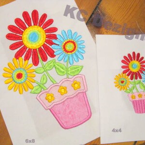 May include: Embroidered design of a pink flower pot with four colorful flowers. The design is available in two sizes: 6x8 inches and 4x4 inches.