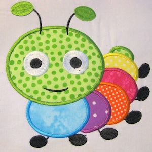 May include: A green and blue embroidered appliqué of a smiling caterpillar with polka dot and floral patterns. The caterpillar has large white eyes with black pupils and a smiling mouth.