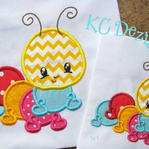 Puede incluir: Diseño bordado de una oruga con patrón de chevron amarillo y blanco, con un cuerpo azul y segmentos de lunares rojos, amarillos y rosas. El diseño está disponible en dos tamaños, 4x4 y 6x6 pulgadas.