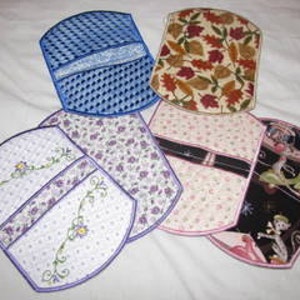 May include: Six different fabric pot holders with various designs. The pot holders are all oval shaped and have a quilted design. The designs include a blue and white checkered pattern, a floral pattern with purple flowers, a pink floral pattern, a brown and beige leaf pattern, a white and purple floral pattern with a green vine, and a black and white pattern with a pink ballerina and a bird.