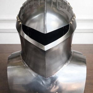 Op de afbeelding: Een gepolijste stalen ridderhelm met vizier en nekbescherming. De helm heeft geklonken accenten en een glad, reflecterend oppervlak. Het ontwerp doet denken aan middeleeuwse harnassen en toont vakmanschap en historische details.