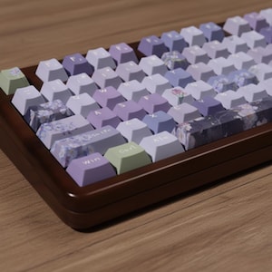 May include: A mechanical keyboard with a wooden frame and pastel-colored keycaps. The keycaps are in shades of lavender, purple, and white, with some featuring floral patterns. The keyboard has a Win, Ctrl, and Alt key.