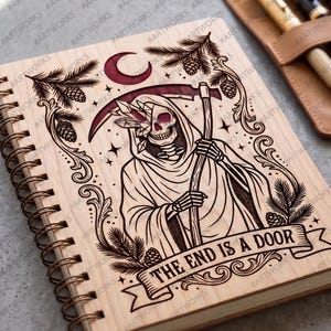 May include: A spiral-bound notebook with a light wood cover featuring a laser-engraved illustration of a skeleton holding a scythe, adorned with crystals and pine branches. A banner at the bottom displays the text, THE END IS A DOOR.