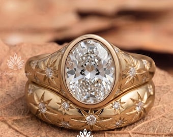 May include: A gold ring set featuring a large oval-cut clear center stone in a bezel setting. The band and the matching contoured band are both decorated with engraved starburst patterns, each containing a small, embedded round clear stone.