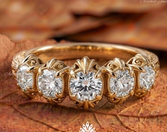 May include: A gold ring featuring five round brilliant-cut white diamonds set in a row. Each diamond is held by ornate, decorative prongs with a textured, vintage-inspired metal band. The ring displays a central stone flanked by four smaller stones.