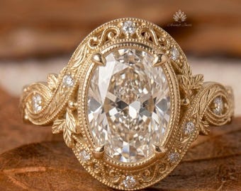 May include: A gold ring with an oval, clear gemstone at its centre. The ring has detailed filigree and small accent stones. The band and setting are decorated with floral and leaf patterns. The ring is set on a brown surface.