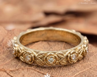 May include: A gold band ring featuring a continuous relief pattern of sculpted roses and leaves. Several small, round, clear faceted stones are set into the centres of the rose motifs, creating a detailed floral design around the entire ring.