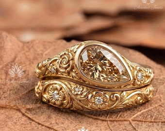 May include: A gold ring set featuring a pear-shaped champagne-coloured centre stone and a matching band. Both pieces are crafted with intricate floral engravings and small embedded round diamonds throughout the metal surface.