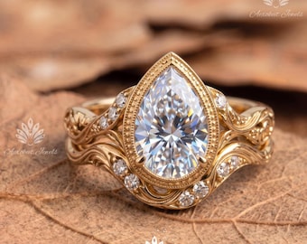 May include: A gold ring featuring a pear-shaped center stone surrounded by a beaded bezel setting. The band displays intricate scrollwork engravings and is accented with small round stones embedded along the sides of the ornate metal shank.