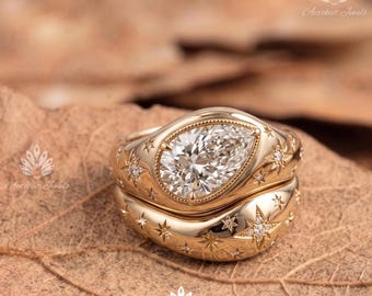 May include: A gold ring set featuring a pear-shaped center stone surrounded by a bezel setting. The band and the matching contoured wedding band are decorated with engraved star motifs, some of which are accented with small, embedded round diamonds.