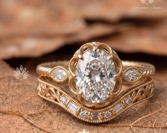 May include: A gold ring set featuring an oval-cut centre stone held in a scalloped setting, flanked by two marquise-cut stones on a twisted band. A curved wedding band with filigree details, small round stones, and baguette-cut stones sits below.