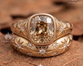 Puede incluir: Un conjunto de anillos de oro con una piedra preciosa central de color champán en talla cojín y engaste de bisel. La banda y el anillo apilable a juego están decorados con patrones de estrellas grabados, cada uno con una piedra clara redonda.