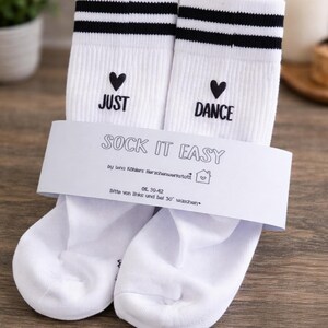 Pu&ograve; includere: Calzini bianchi con strisce nere e le parole "JUST" e "DANCE" con cuori. La confezione dice "SOCK IT EASY". Taglia 39-42.