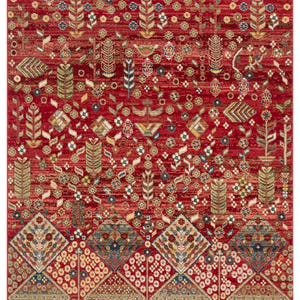 Peut inclure: Un tapis rouge avec un motif floral et g&eacute;om&eacute;trique complexe. Le tapis pr&eacute;sente un fond rouge profond avec des motifs d&eacute;taill&eacute;s dans des tons de bleu, beige et vert. La bordure pr&eacute;sente un motif de losanges.