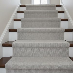 Puede incluir: Una escalera con escalones alfombrados de color gris claro y detalles en madera oscura. Los escalones están enmarcados por contrahuellas blancas y una barandilla blanca. Diseño limpio y moderno, adecuado para la decoración del hogar.