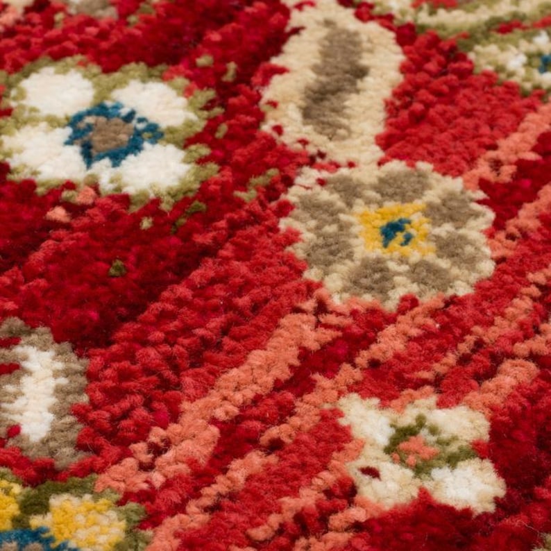 Peut inclure: Gros plan sur un tapis rouge &agrave; motifs floraux. Le tapis pr&eacute;sente une surface textur&eacute;e avec des motifs floraux blancs, beiges, jaunes et bleus. Le fond est rouge fonc&eacute;, avec des touches d'orange et de p&ecirc;che.