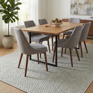 May include: A dining room set featuring a rectangular wooden table with a black metal base, surrounded by six gray upholstered chairs with wooden legs. The table is set on a gray and white patterned rug, with a large potted plant and artwork in the background.