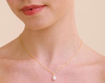 May include: A woman wearing a white strapless wedding dress with a pearl necklace. She has her hair pulled back in a bun and is looking at the camera.
