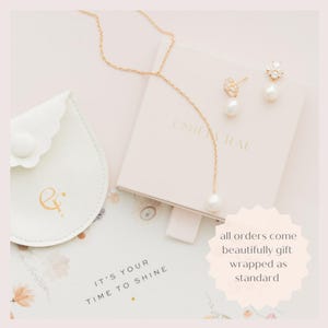 May include: A gold-colored necklace with a single pearl pendant and matching earrings with pearl drops are displayed on a light pink box. A small, white, scalloped pouch with gold lettering and the text "IT'S YOUR TIME TO SHINE" are also visible.