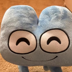 May include: A light blue plush toy in the shape of the number four, featuring large, round eyes and a smiling mouth. The eyes have white centres with black outlines and curved black pupils. The plush is made of a soft, fuzzy material.