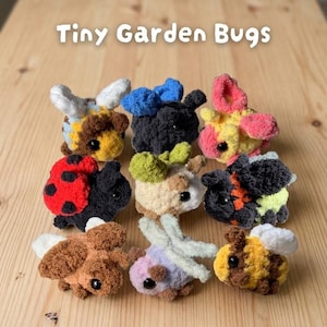 May include: A collection of nine crocheted garden bugs in various colors, including bees, ladybugs, and dragonflies. The text "Tiny Garden Bugs" is displayed at the top. The bugs are arranged on a light brown wooden surface.