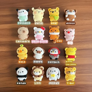 Może przedstawiać: Kolekcja szesnastu szydełkowych figurek zwierząt, w tym pandy, lwa i tygrysa. Każda figurka jest w jasnych kolorach i ma charakterystyczne cechy, z nazwami takimi jak "Hello Kitty" i "Winnie the Poon".