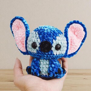 Pu&ograve; includere: Un peluche all'uncinetto blu e bianco fatto a mano con grandi orecchie foderate di rosa e occhi neri. Il peluche &egrave; un personaggio di un popolare film d'animazione. Il giocattolo &egrave; tenuto in una mano.