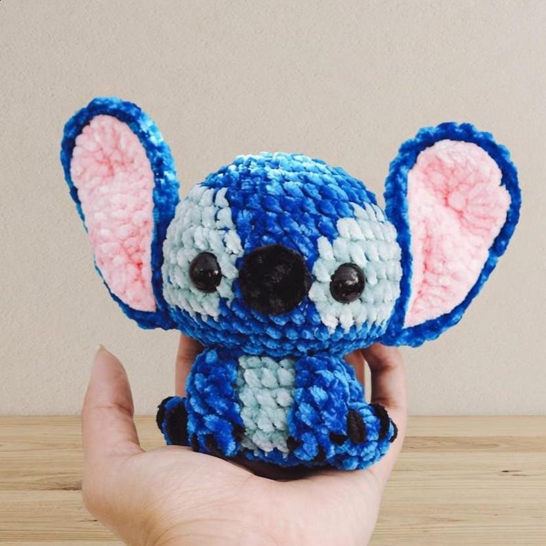 Pu&ograve; includere: Un peluche all'uncinetto blu e bianco fatto a mano con grandi orecchie foderate di rosa e occhi neri. Il peluche &egrave; un personaggio di un popolare film d'animazione. Il giocattolo &egrave; tenuto in una mano.
